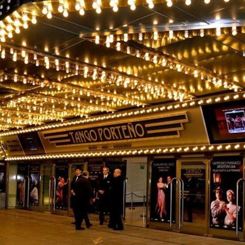 مدخل مسرح مضاء مع لافتات "تانجو بورتينو"، وملصقات للراقصين، وأشخاص يرتدون ملابس رسمية يقفون بالخارج.