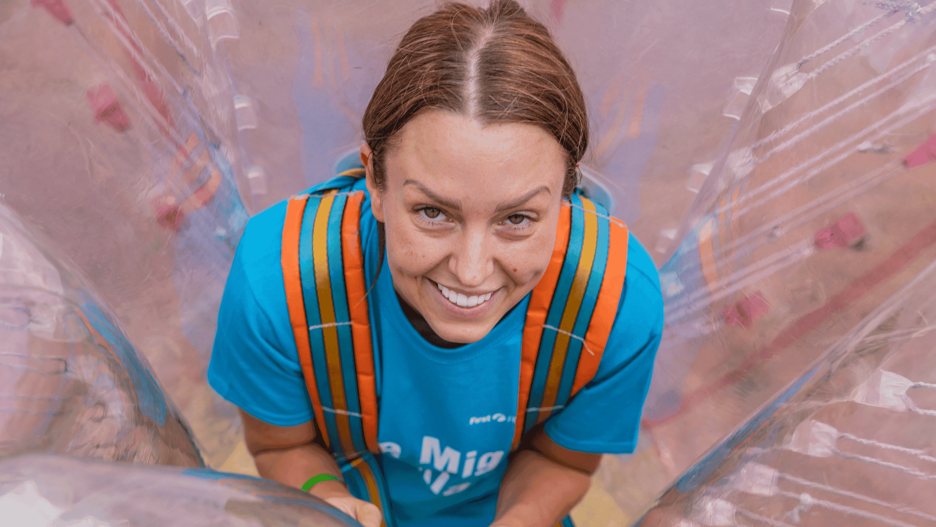 Outdoor team-building event with participants wearing matching blue shirts, taking part in inflatable obstacle courses and games, smiling and cheering, with the words 'ENTER A TEAM' in large bold white and green text across the image.
