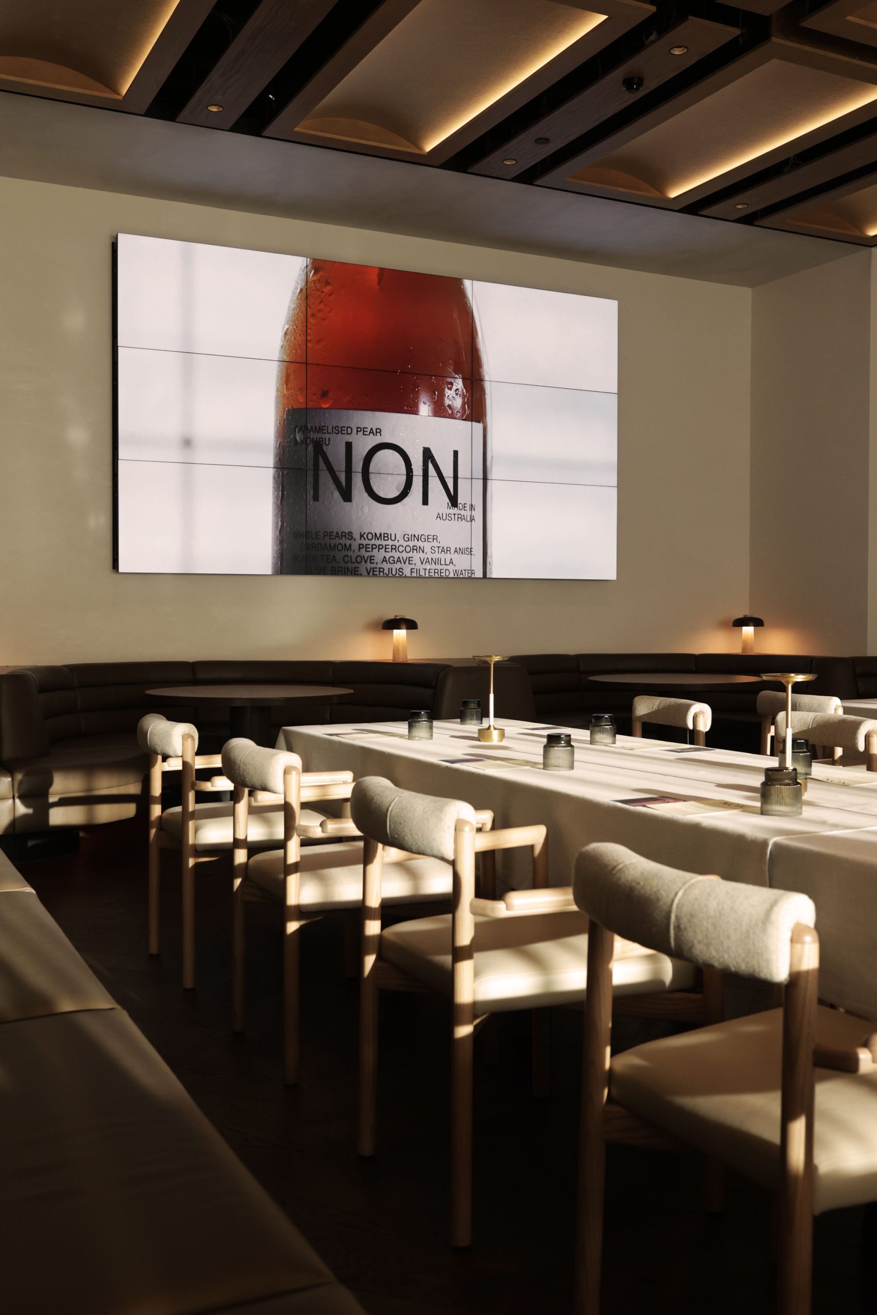 Dining room set for an event with a large screen displaying a "NON" non-alcoholic wine bottle labelled "Caramelised Pear & Kombu"