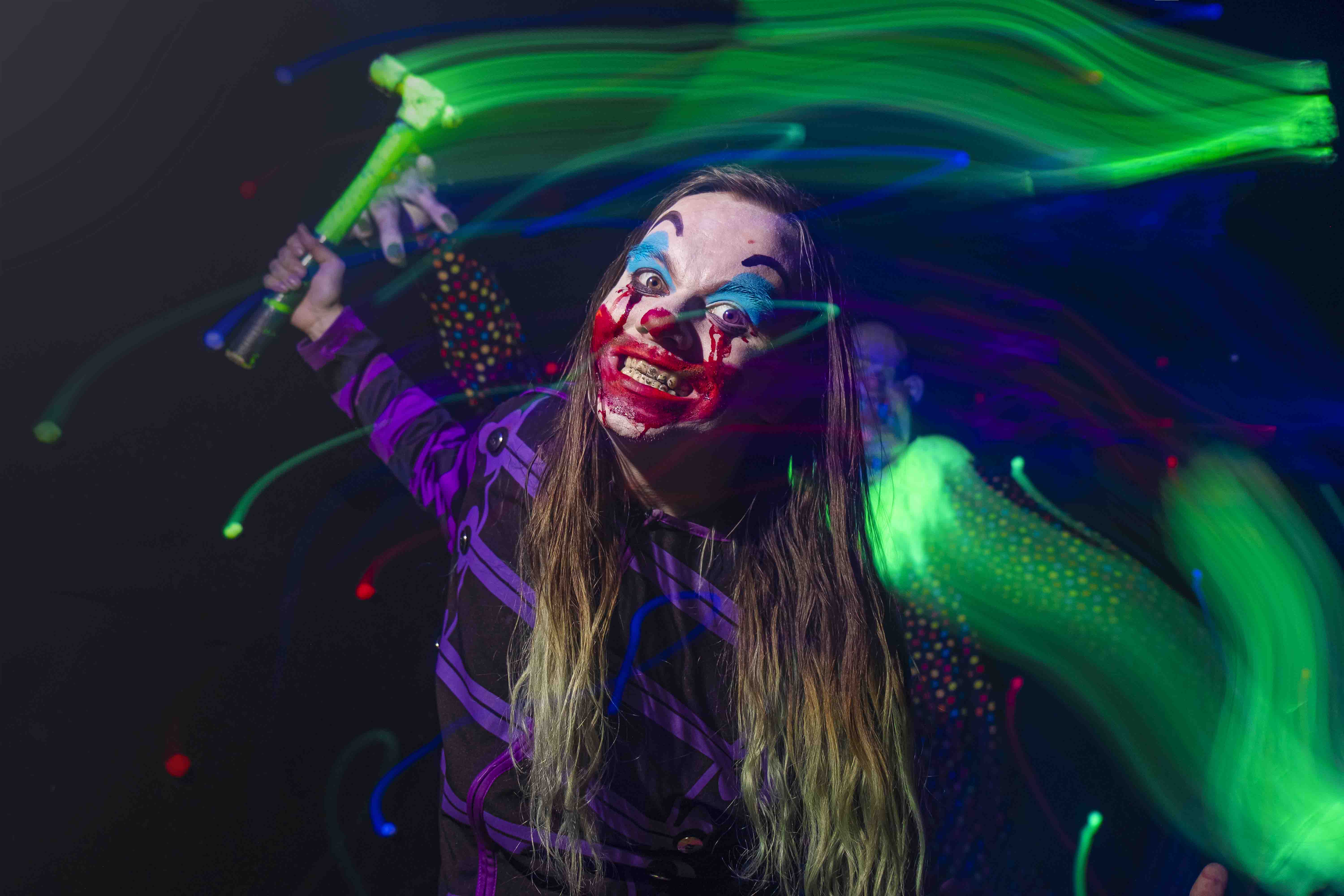 A performer with long hair dances with colorful light trails in a dark setting, creating a vibrant atmosphere.
