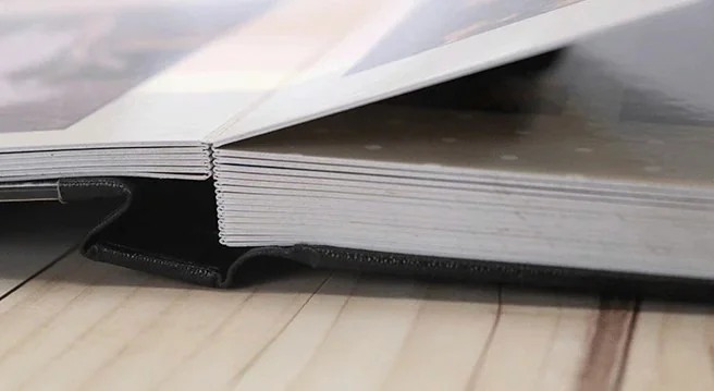 Mãos segurando fotolivro com capa personalizada de duas mulheres sorrindo, com a frase “Eu amo o Nordeste”, sobre mesa de madeira e flores decorativas