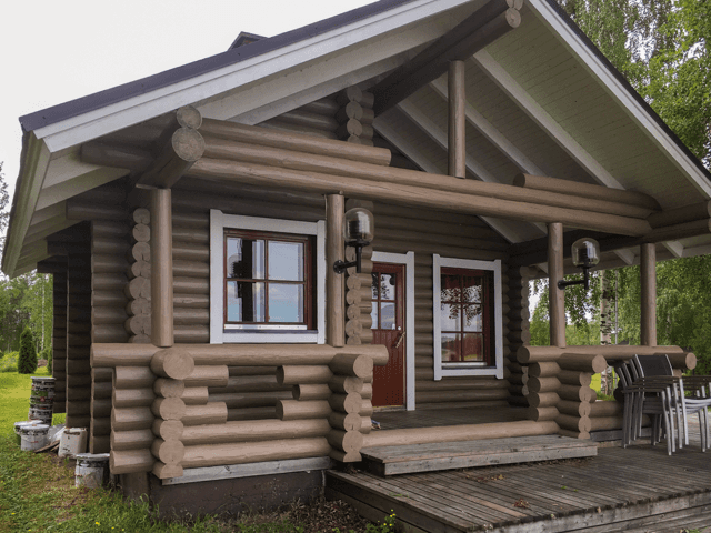 Ulkomaalattu tumma hirsimökki Lappajärvellä, katettua kuistia ja puuverhoilua, luonnonläheinen pihapiiri