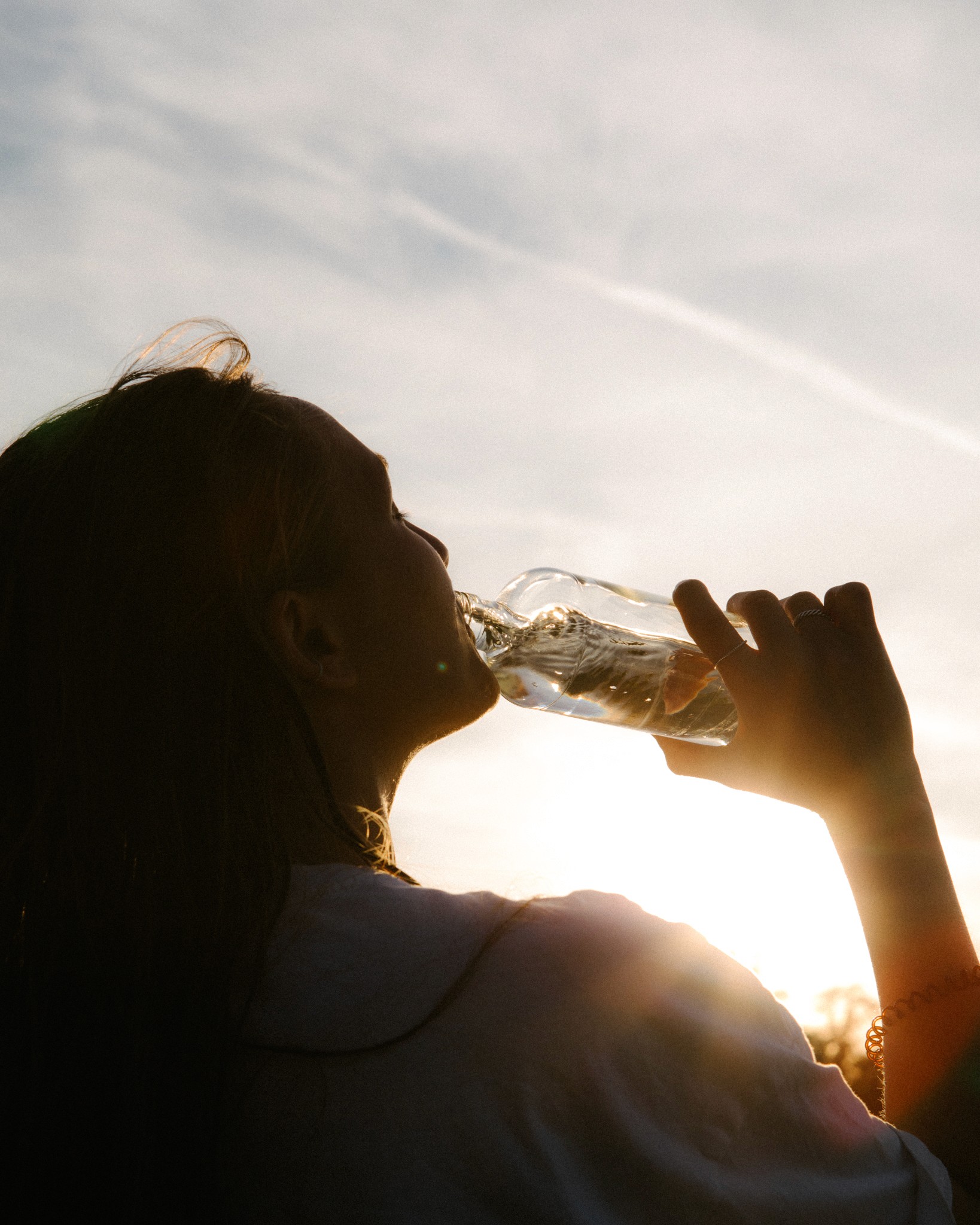 Frau trinkt Wasser aus Glasflasche im Sonnenlicht