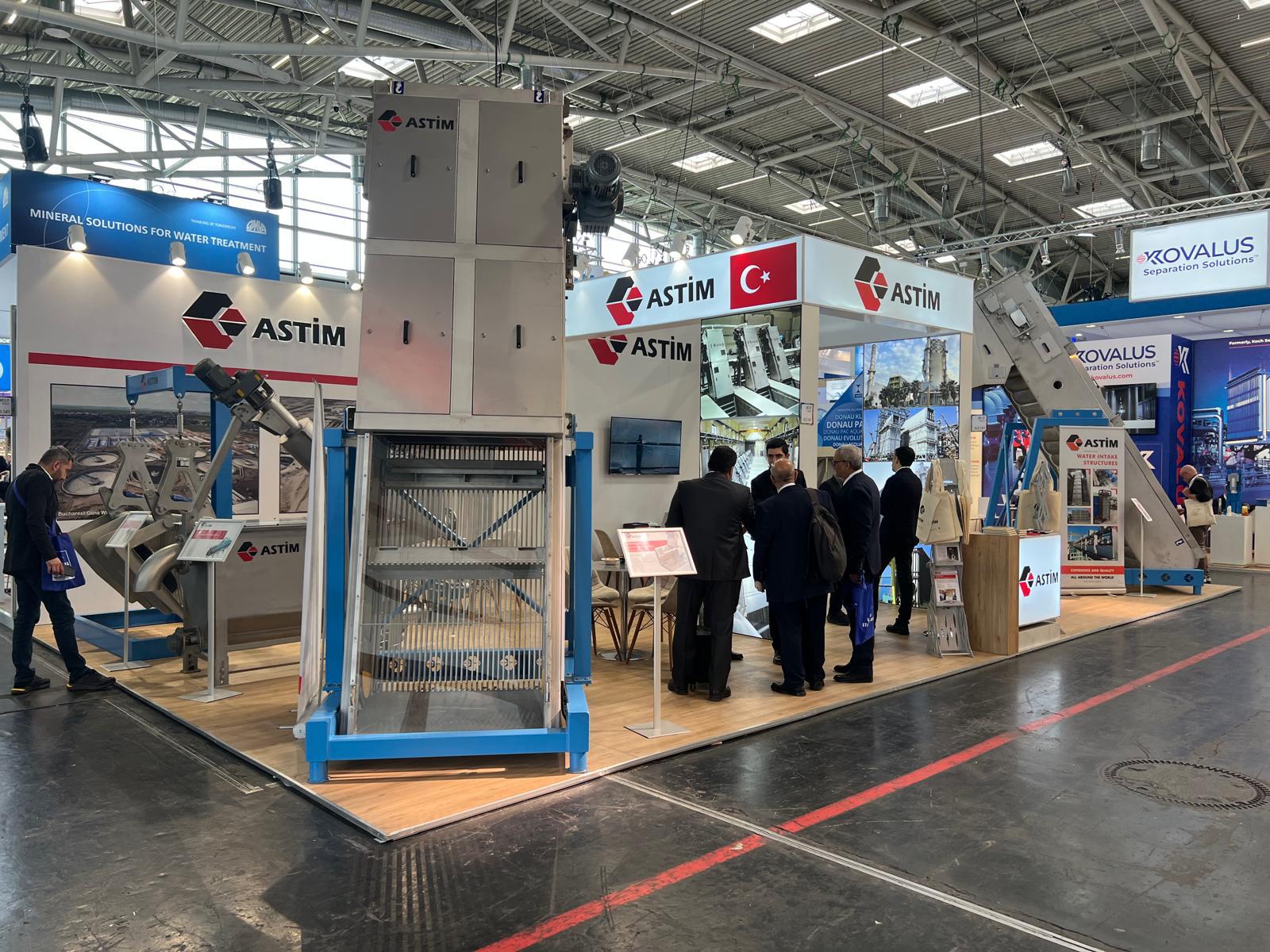 ASTIM exhibition stand at IFAT 2026 Munich, featuring large industrial machine displays and graphic panels.