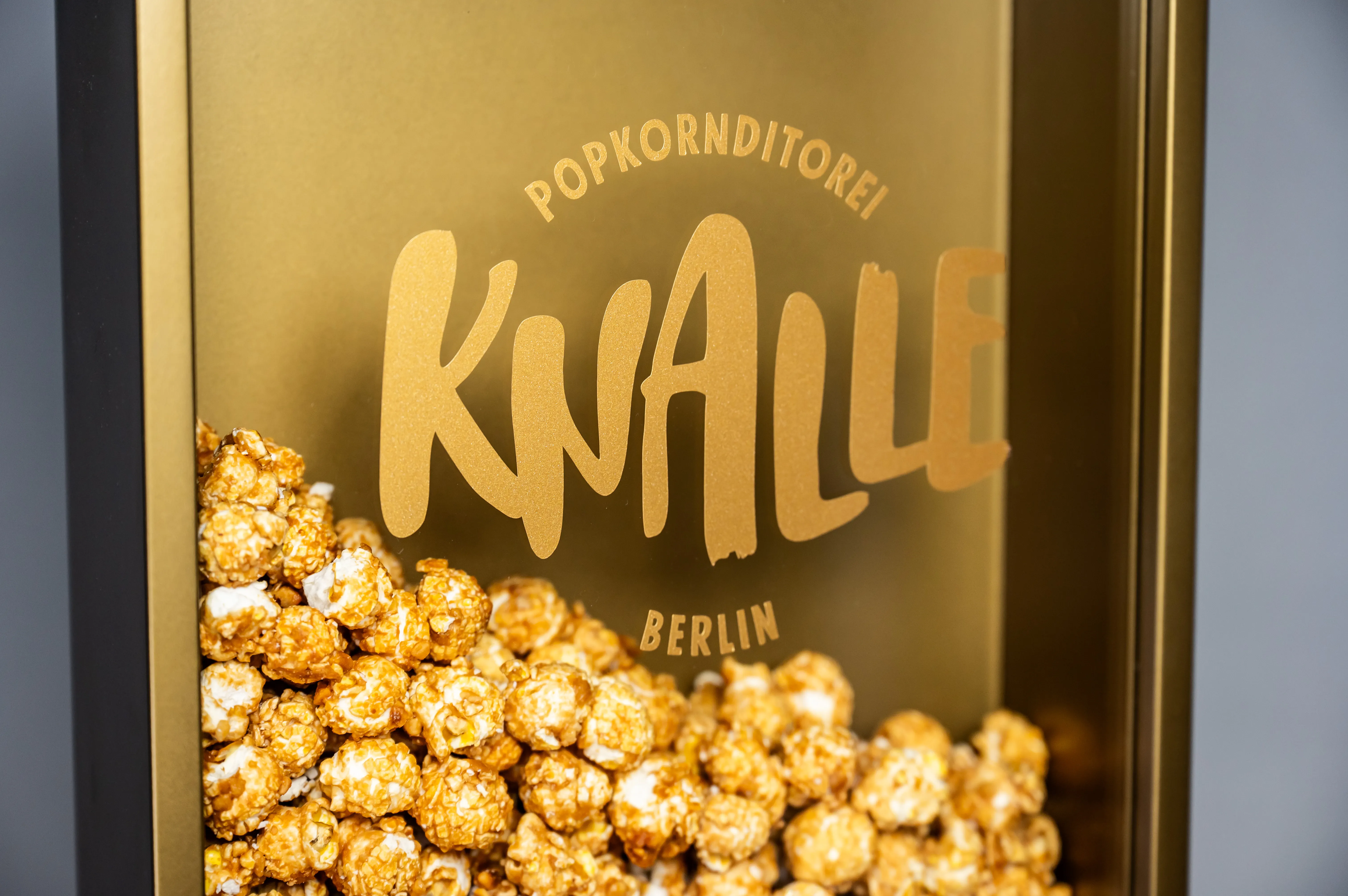 Detail of the golden KNALLE Popkornditorei Berlin showcase filled with caramel popcorn behind glass.