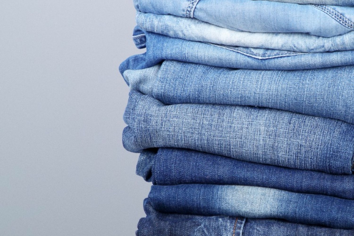 A neatly stacked pile of folded denim jeans in various washes and shades, showcasing versatile styles for personal styling, colour analysis and wardrobe building