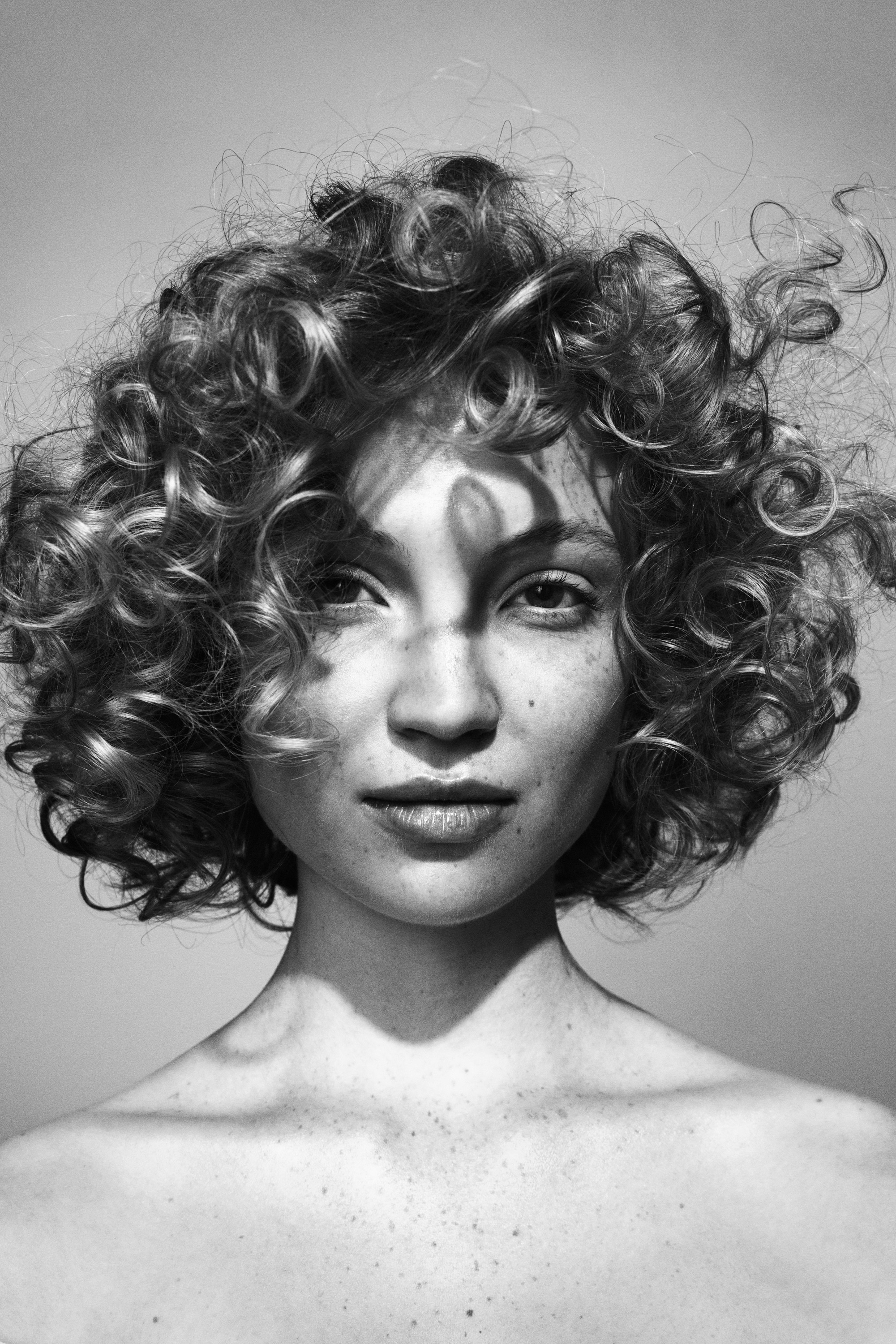A black and white beauty photo of a fair model with freckles and very curly hair that frames her face.