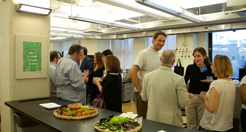 A photo of a group of people sitting in an office room and talking near a bouffe.