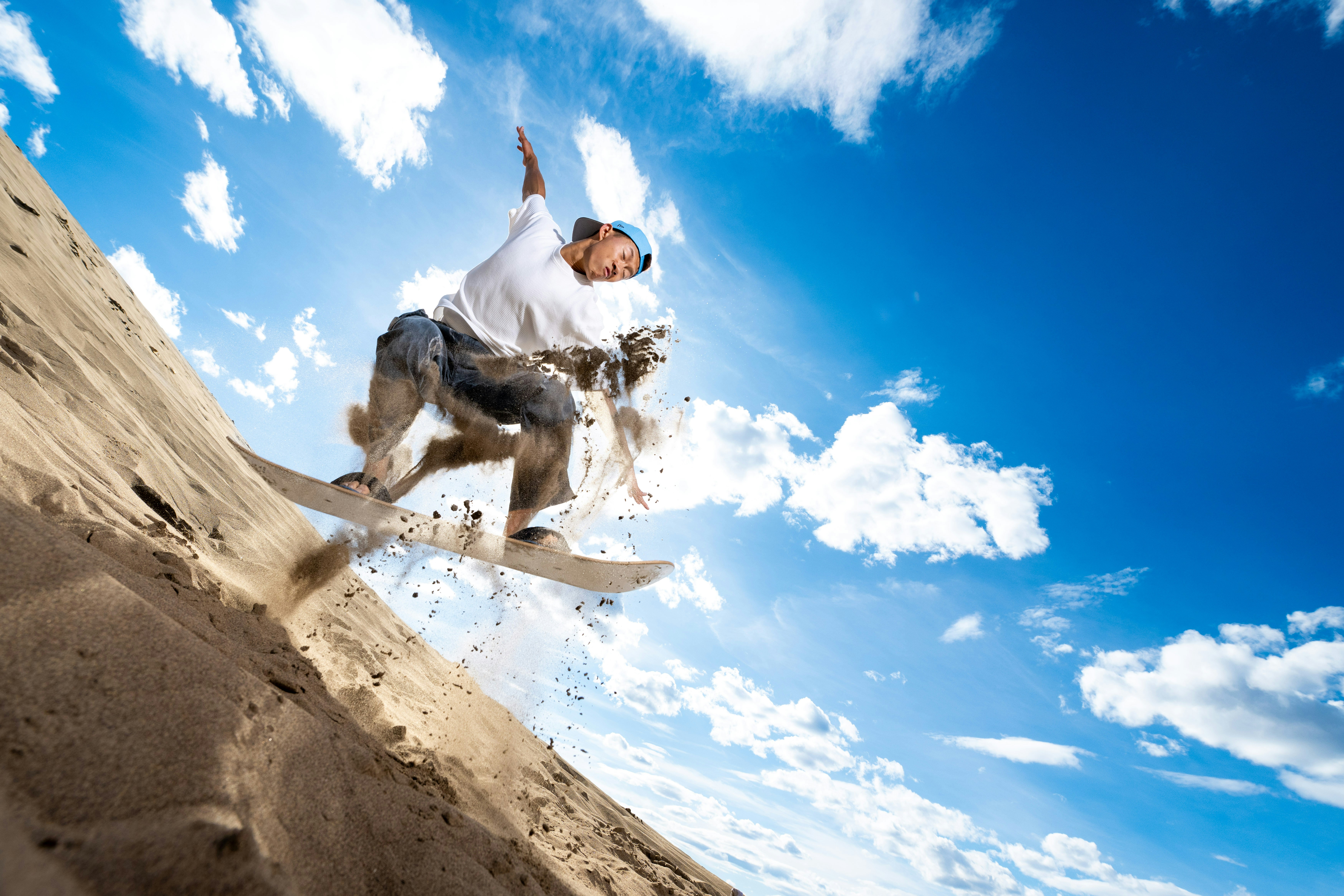 Man sandboarding on a dune against a bright blue sky.