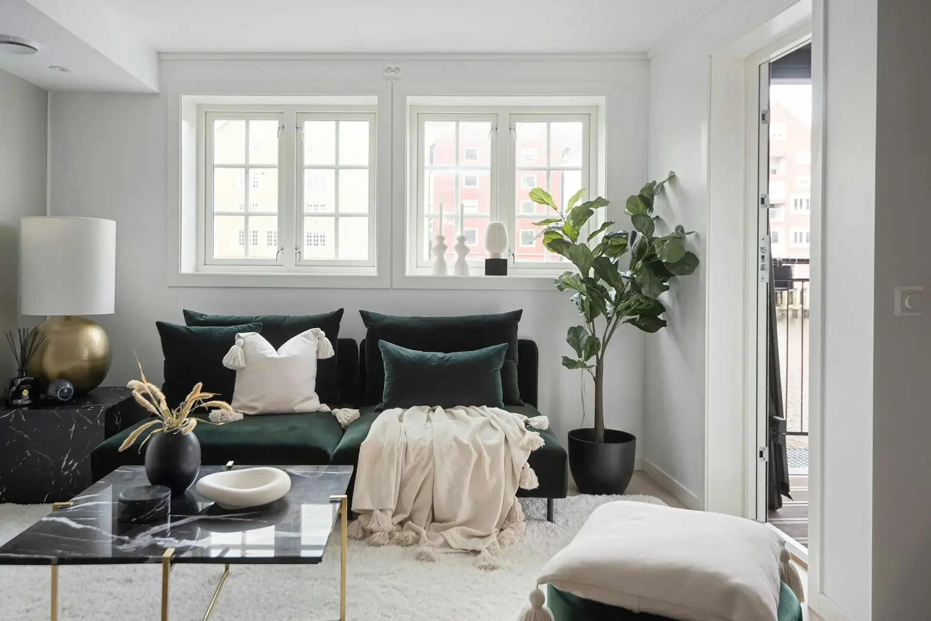 Bright living room with green sofa, marble coffee table, indoor plant, and large windows.