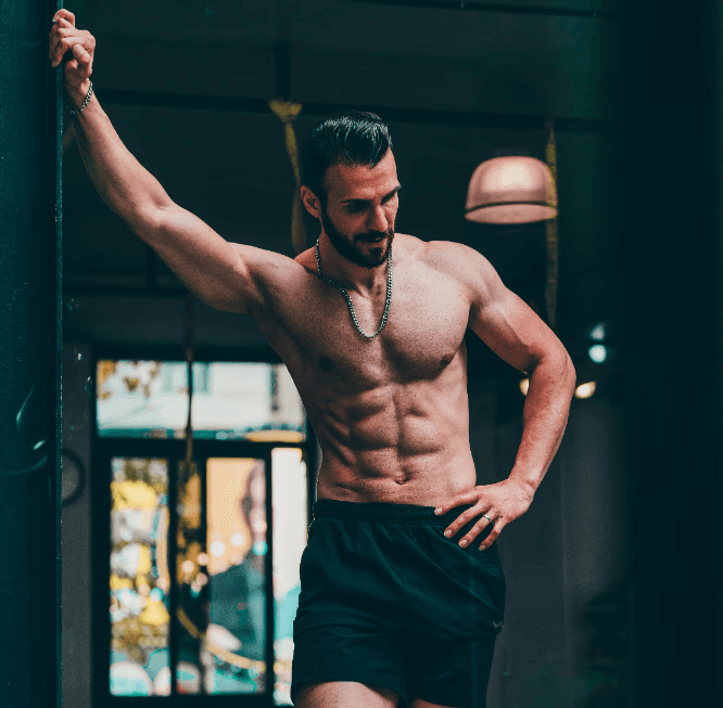 A shirtless man flexing outdoors next to gym equipment, pointing upward. Text: Ethan Brooks – Strength Coach.