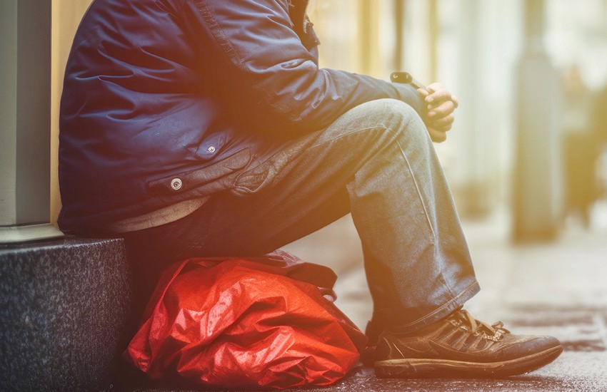 Person sitting on a city street beside a red bag, highlighting street homelessness