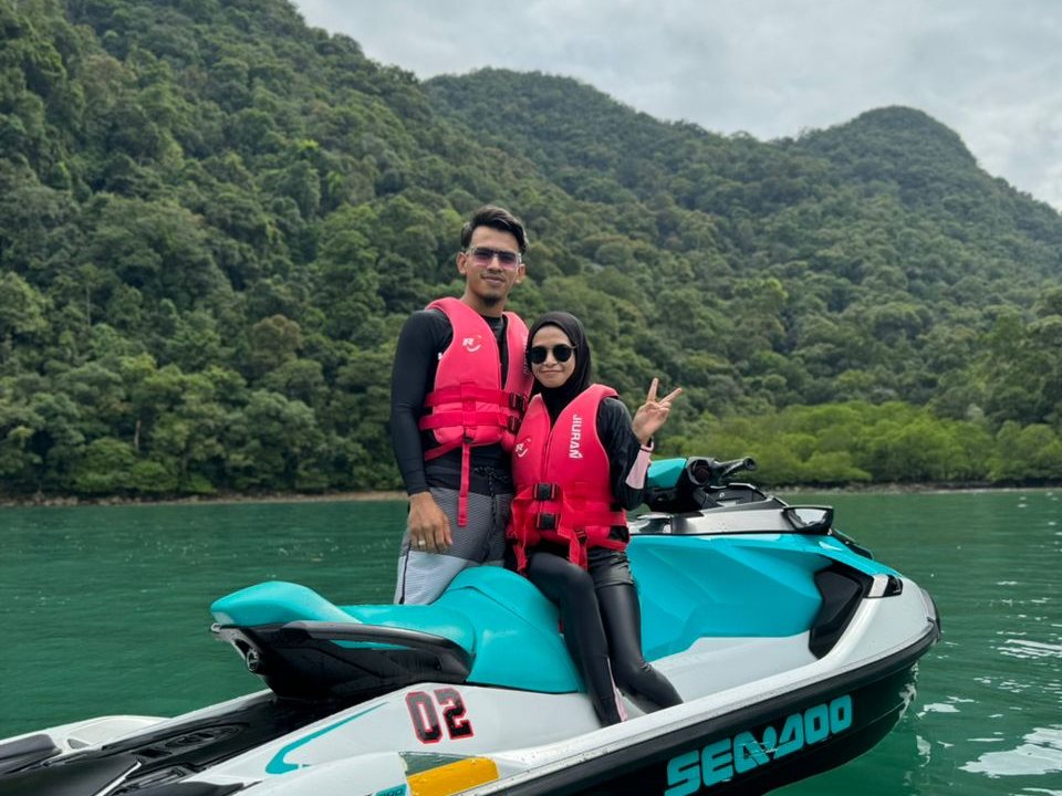 Two guests on a jet ski stopped below the forested hills of the southern islands