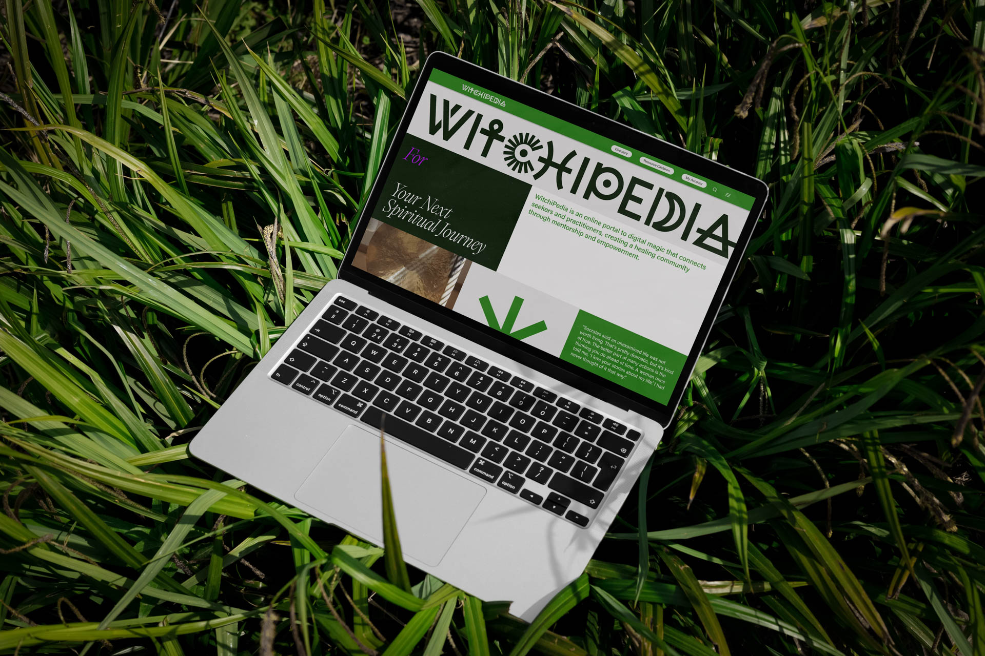 A silver laptop rests open on green grass. The laptop screen displays the Wikipedia logo and the tagline "Your Next Spiritual Journey." The keyboard is visible, and the laptop is angled slightly. The background consists of long, blade-like green grass.