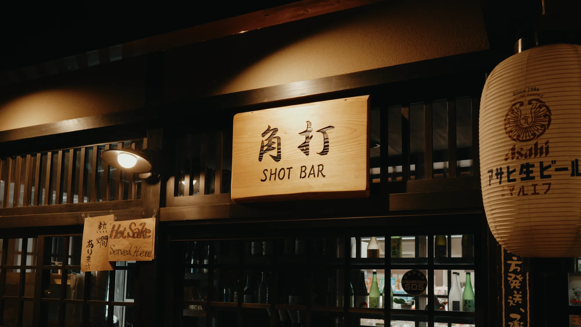 A dark timber shopfront at night with a kakuuchi shot bar sign and lit Asahi lantern