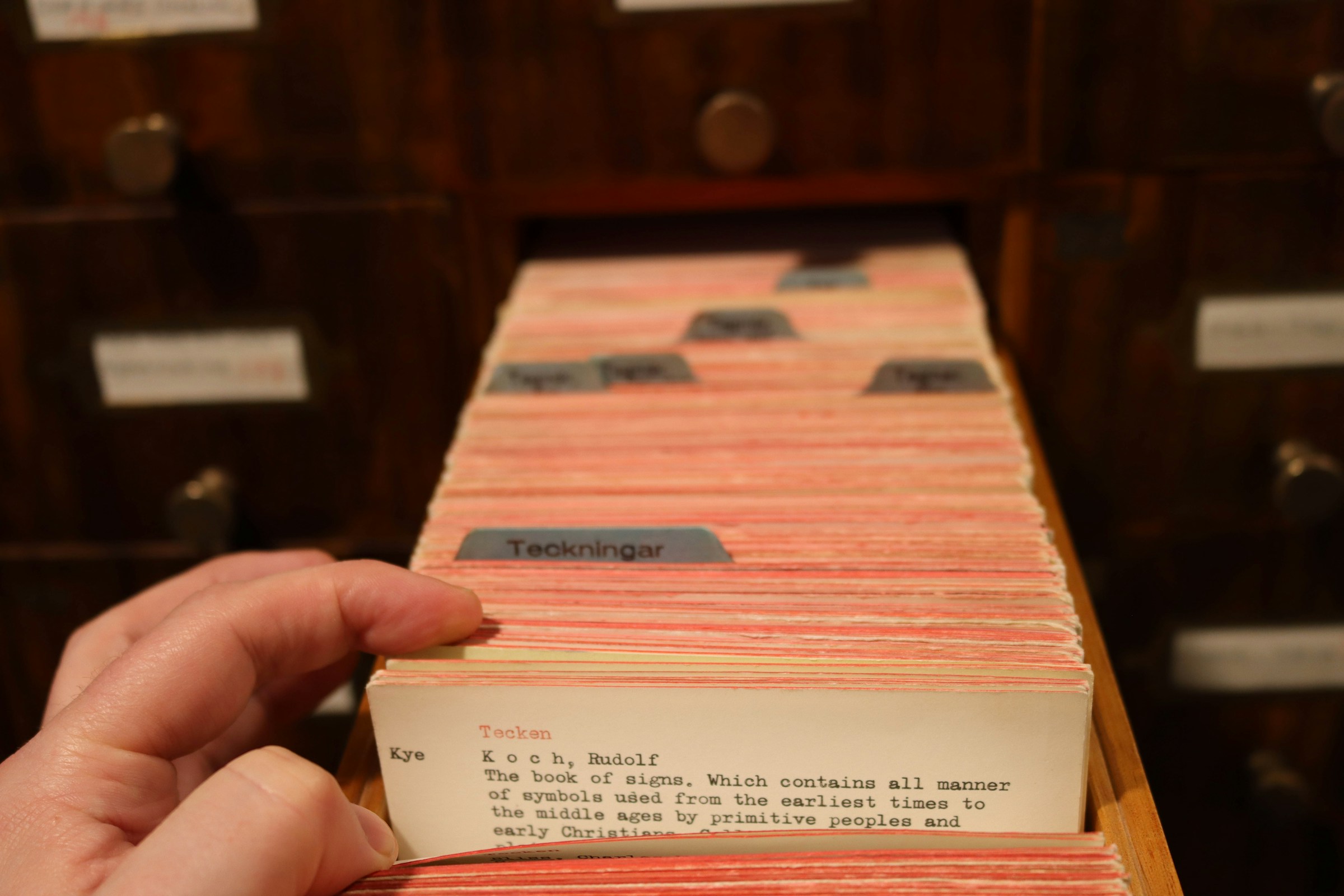 A hand pulling a card from a library card catalogue