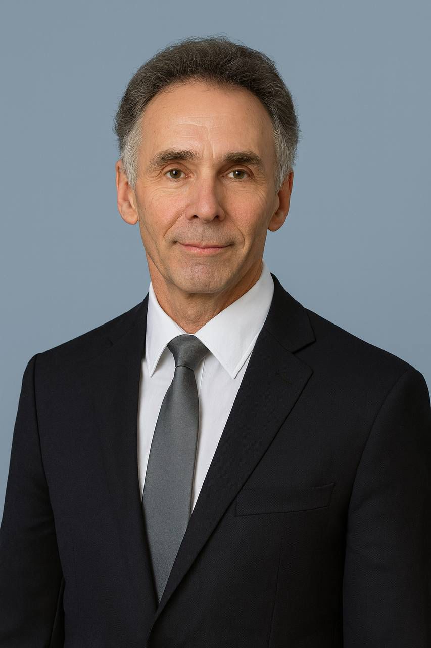 Portrait of a woman with long, smooth hair swept to the side, in a dark t-shirt, on a plain background.