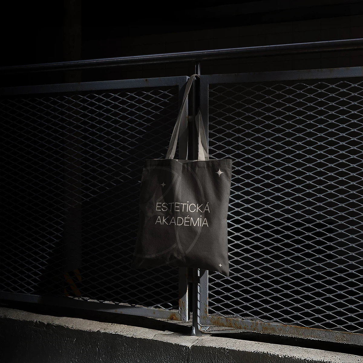 A black tote bag hanging on a wire fence in a dimly lit setting.