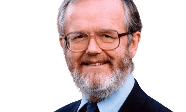 Color portrait of a middle-aged man with a full beard and glasses, smiling warmly. He is dressed in a suit jacket and tie, with a natural outdoor background in soft focus. His friendly expression and neatly groomed appearance convey approachability and professionalism.