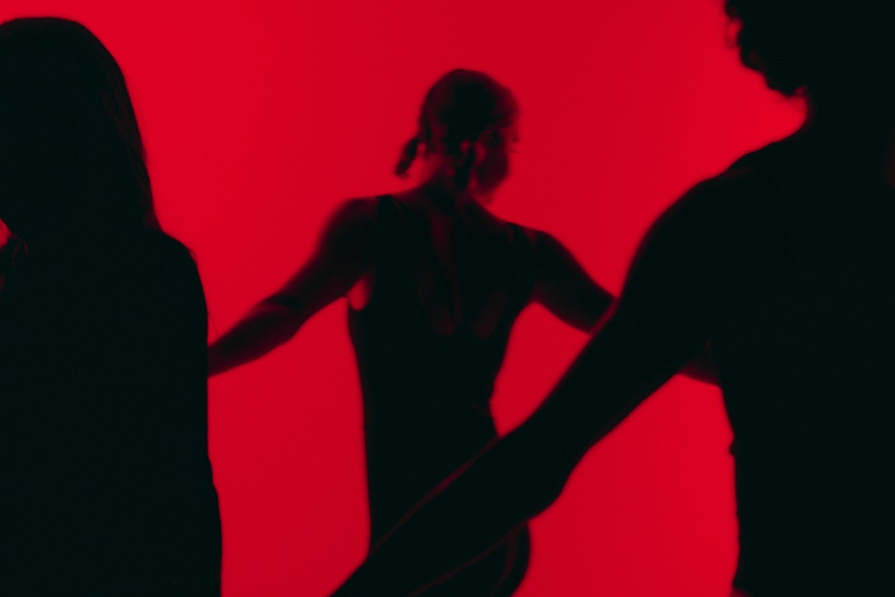 Blurred silhouettes of people in motion against a bold red backdrop.