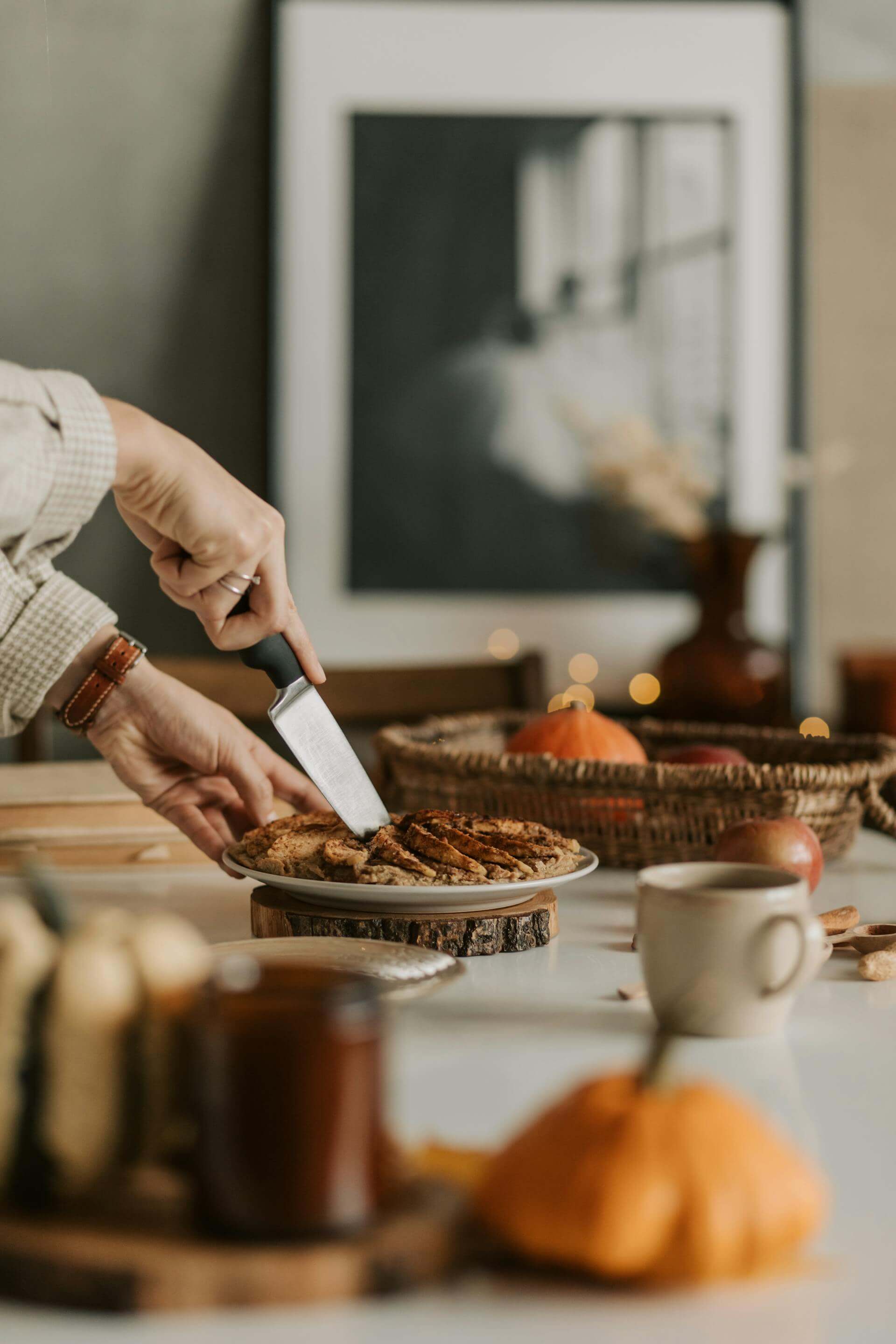 A woman slices a pumpkin pie on a table, showcasing the dessert's golden crust and rich filling