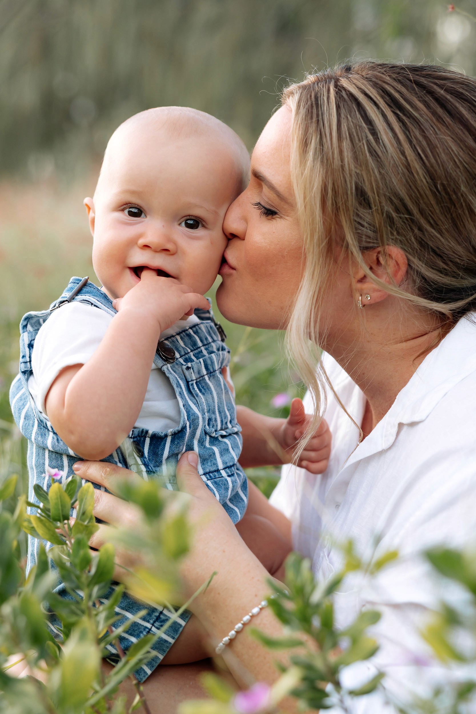Close-up of mum kissing her baby’s head in an open grassy paddock, golden hour motherhood session