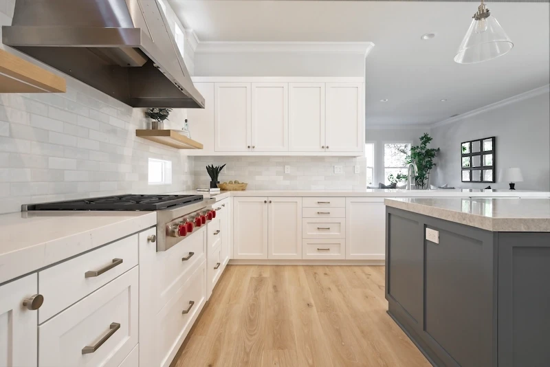 Luxurious kitchen featuring contrasting gray island, white shaker cabinets, tile backsplash, and oak flooring in Bonita Canyon Remodel.