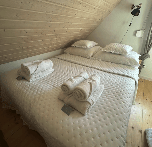 A stylish split-level loft room with an elevated queen bed, modern writing desk below, and floor-to-ceiling windows framing a glowing sunset.