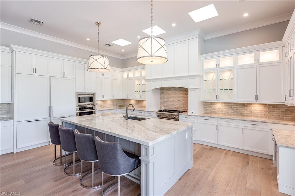 a warm kitchen with white cabinets and hanging lights over a marble counter
