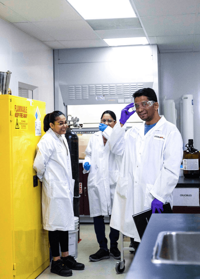 A team of three SteriMax scientists huddling together and smiling in a laboratory.