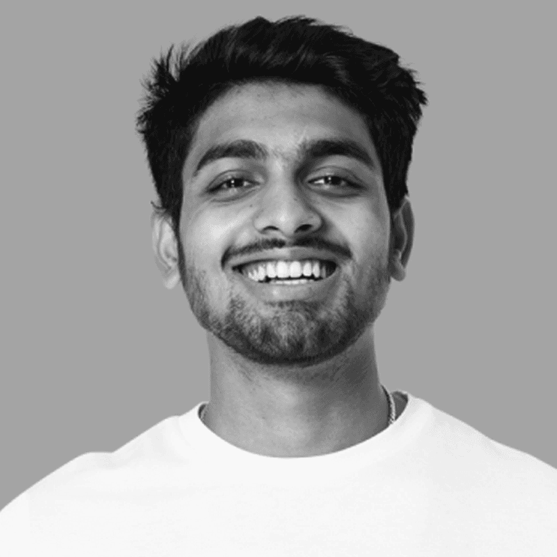 A man reading from a tablet in a collaborative office environment. Desks with documents and a discussion between colleagues are visible in the background.