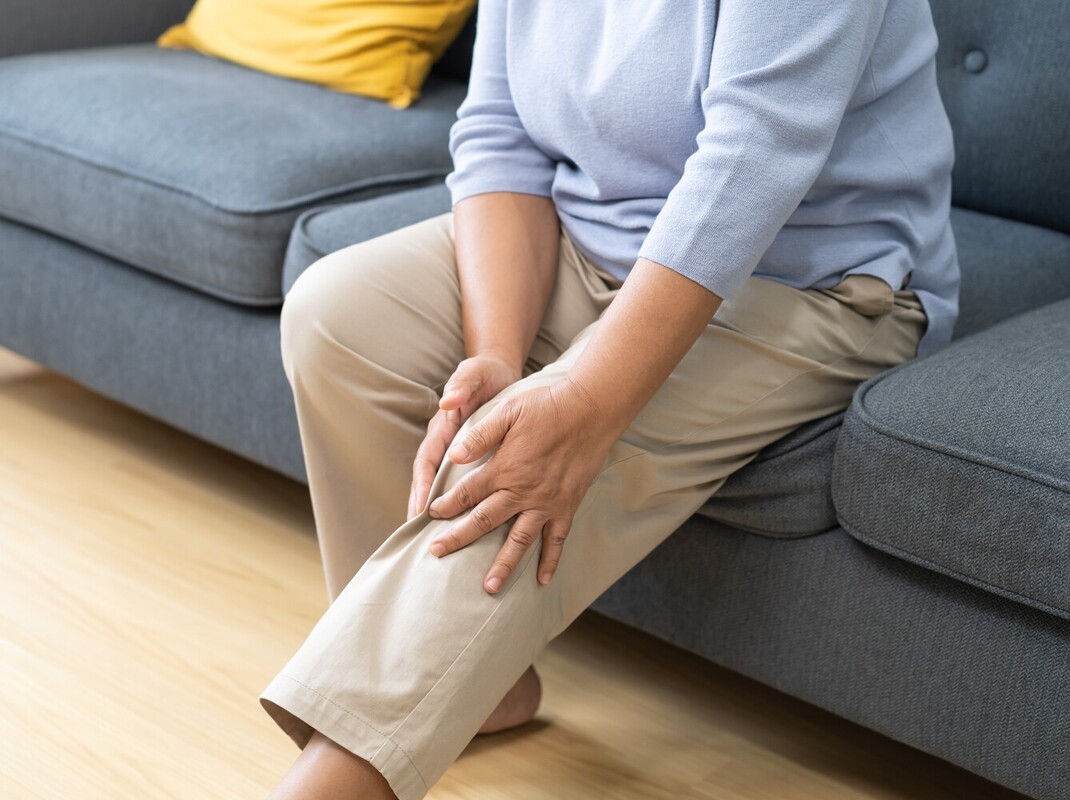 woman sitting on a couch holding her sore leg after exercising too hard during a beginner treadmill workout for weight loss