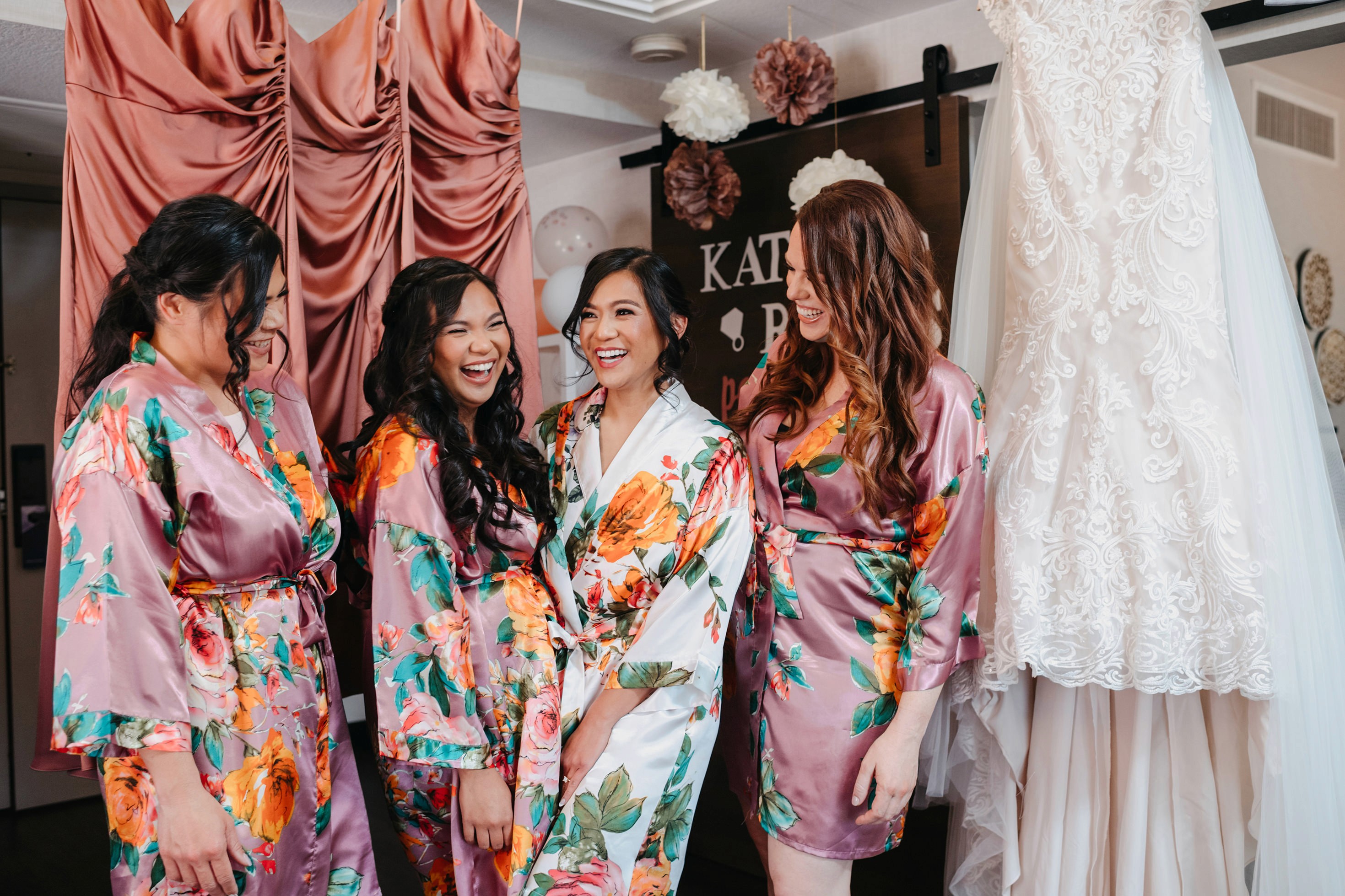 Bridesmaids in floral robes celebrating with the bride during wedding morning prep