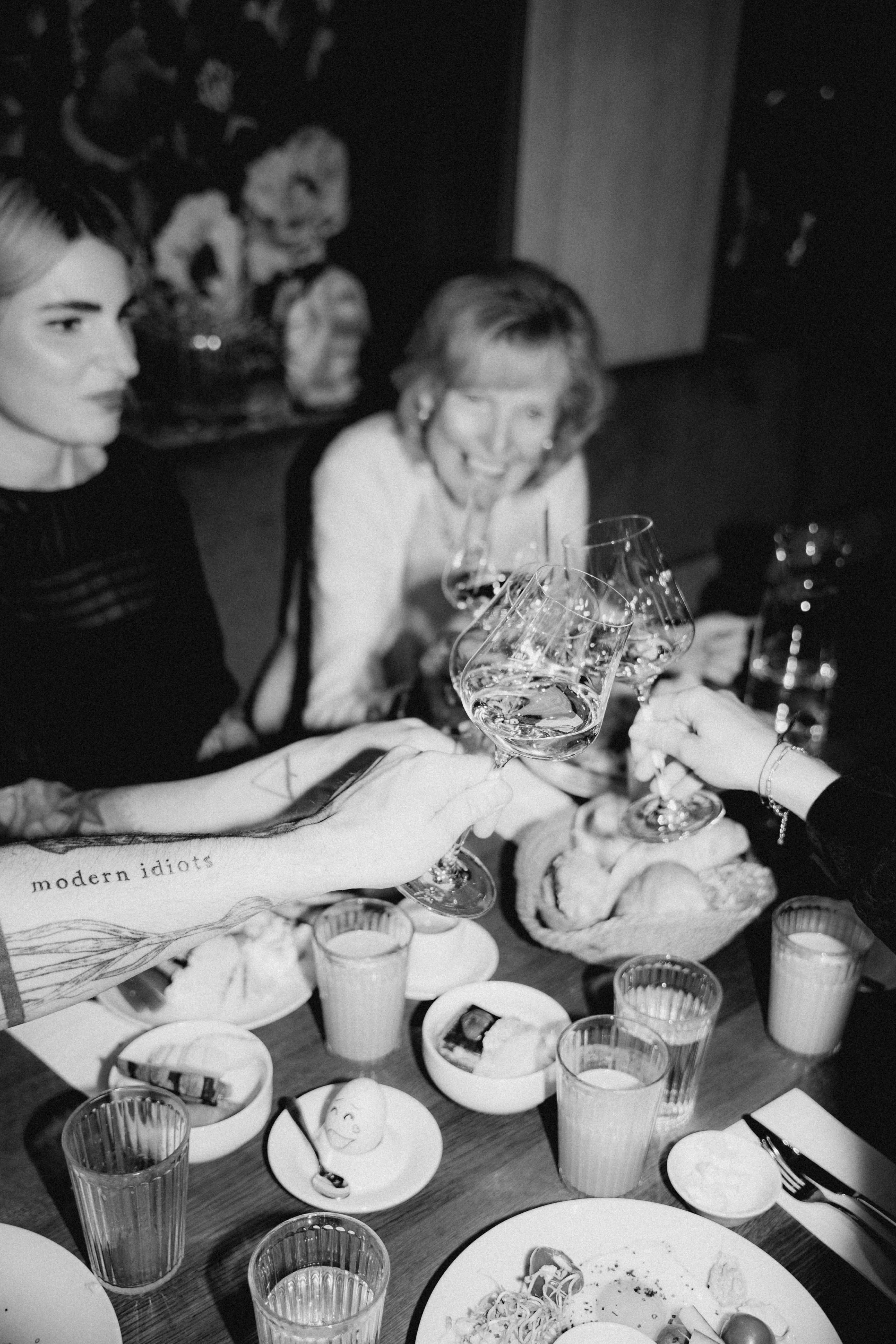 Black and white image of two women at a dining table filled with food and beverages, engaged in conversation.