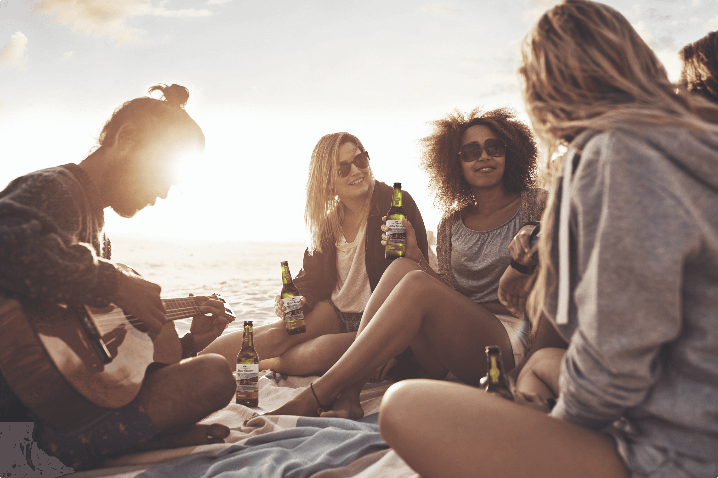 Friends relax on beach, one plays guitar.