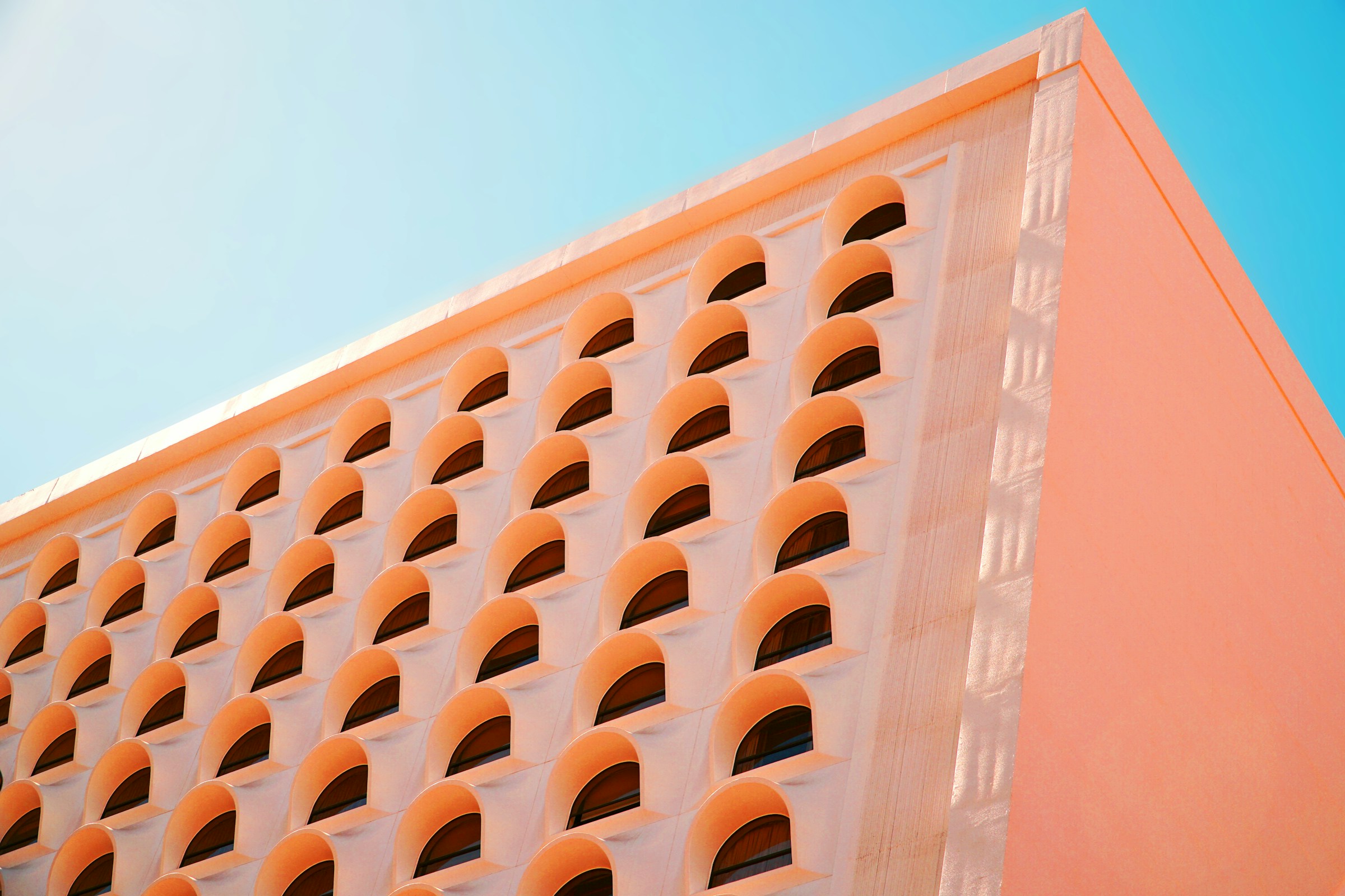 Low-angle editorial photograph of a peach-toned arched building facade against a blue sky