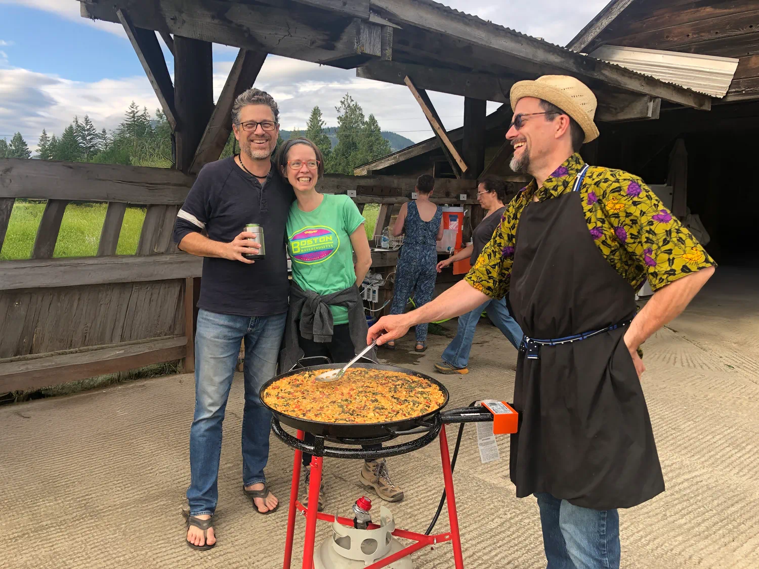 People gathered outdoors while someone cooks food on a large pan at a community event.