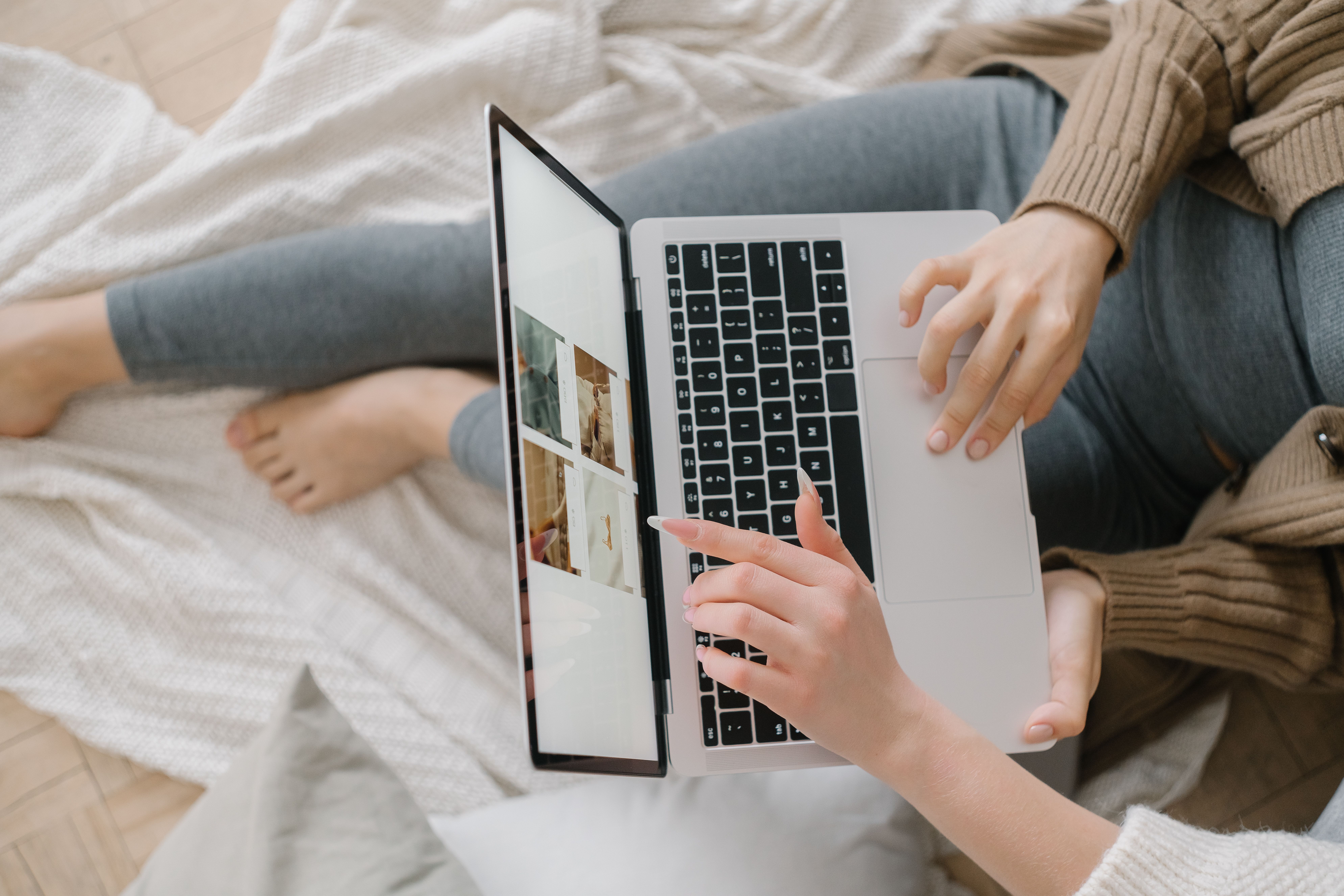 A woman leans on a cozy bed using a laptop, browsing images. Indoor setting.