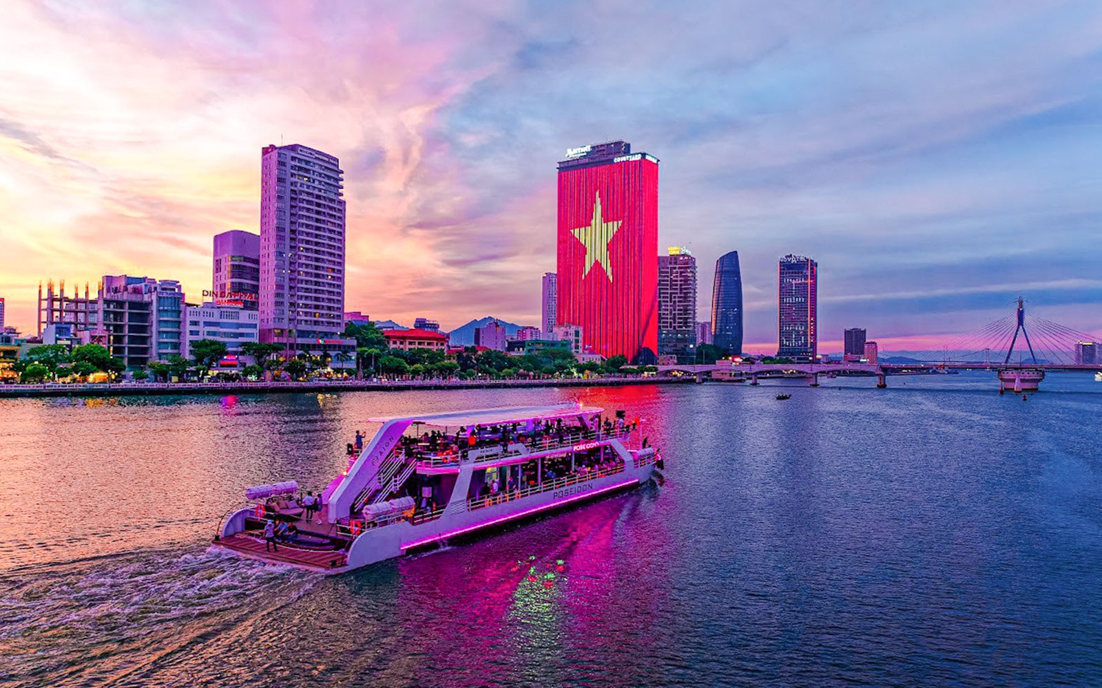 Poseidon cruise on Han River with Da Nang skyline at sunset.