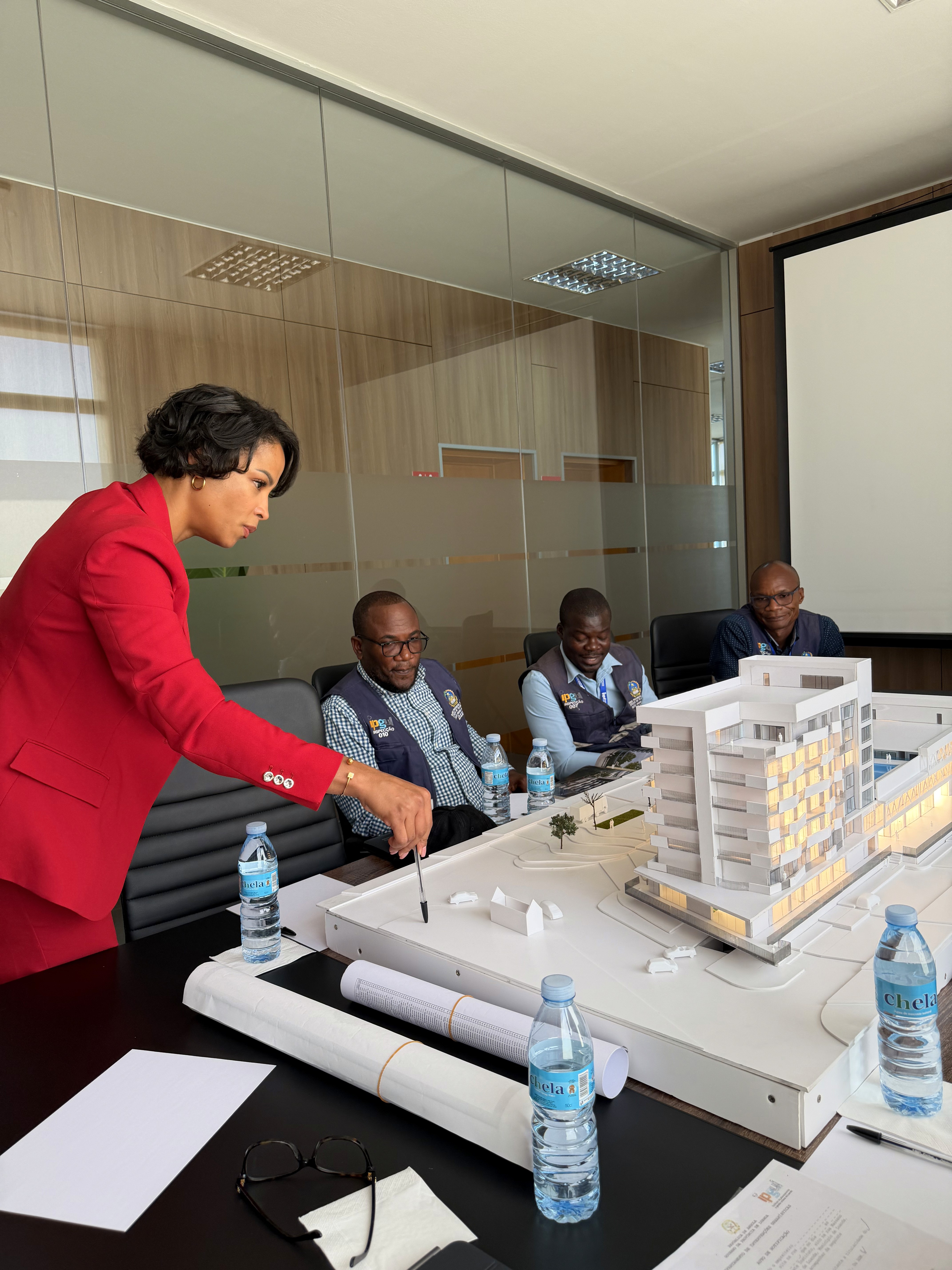 explaining the construction at a meeting: woman in red clothing standing and builders seated.