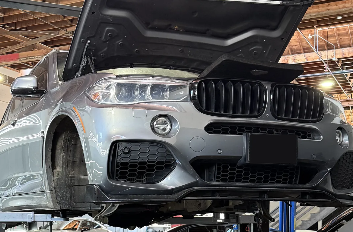Silver BMW SUV raised on a lift with its hood open in the workshop