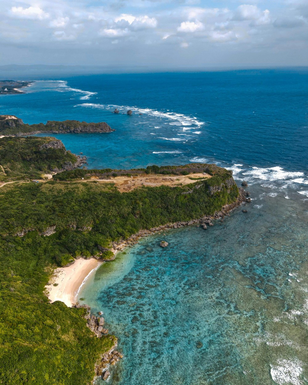 Aerial view of a lush green peninsula with turquoise coral reef waters in Okinawa, Japan