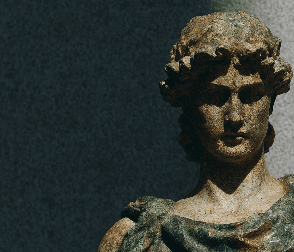 A weathered stone bust with curly hair and draped fabric, partially illuminated by strong sunlight, against a dark.