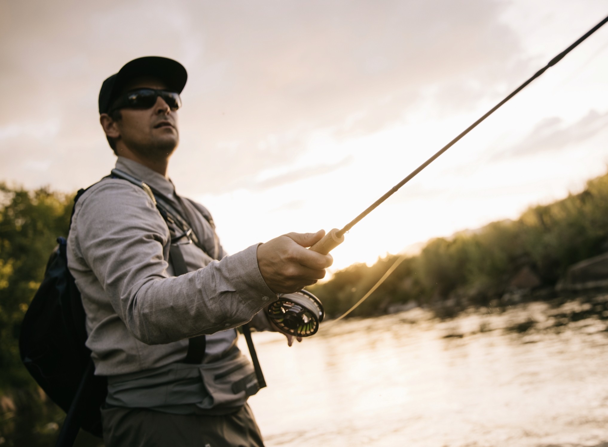 man casting fly fishing rod on beautiful river sunset