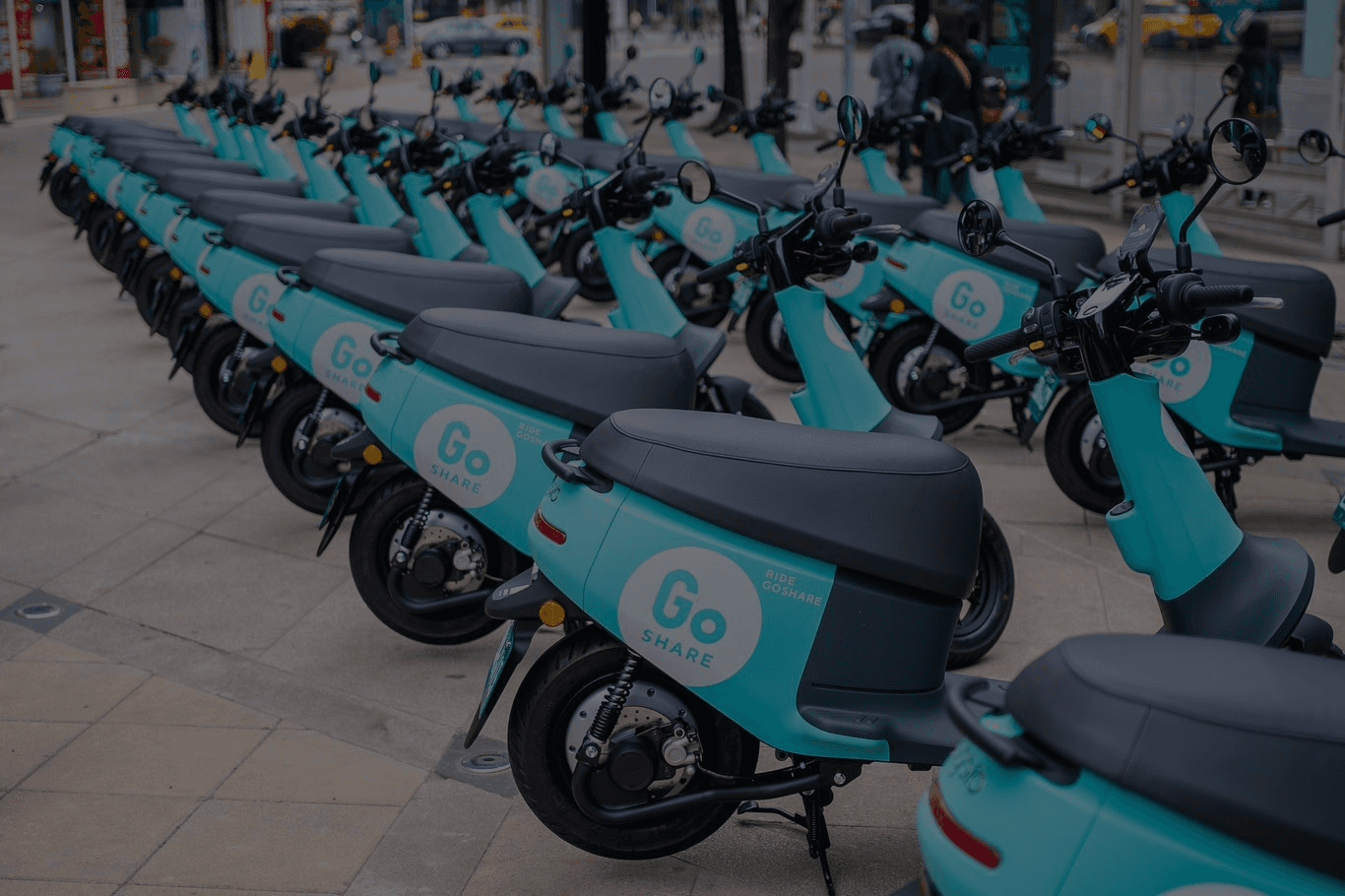 A modern hallway features vibrant teal and orange geometric and leaf patterns, with glossy tiled floors, a large rectangular light fixture, and a small shelf holding a potted plant, all leading to a large, frosted window at the end.
