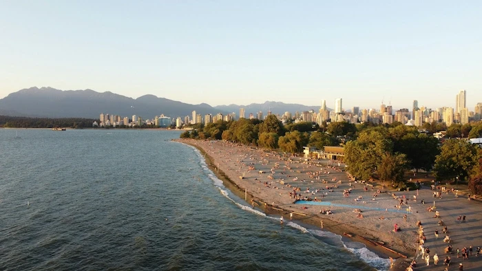 Kitsilano Beach in Vancouver with sandy shoreline, people on the beach, ocean, and skyline in the distance.