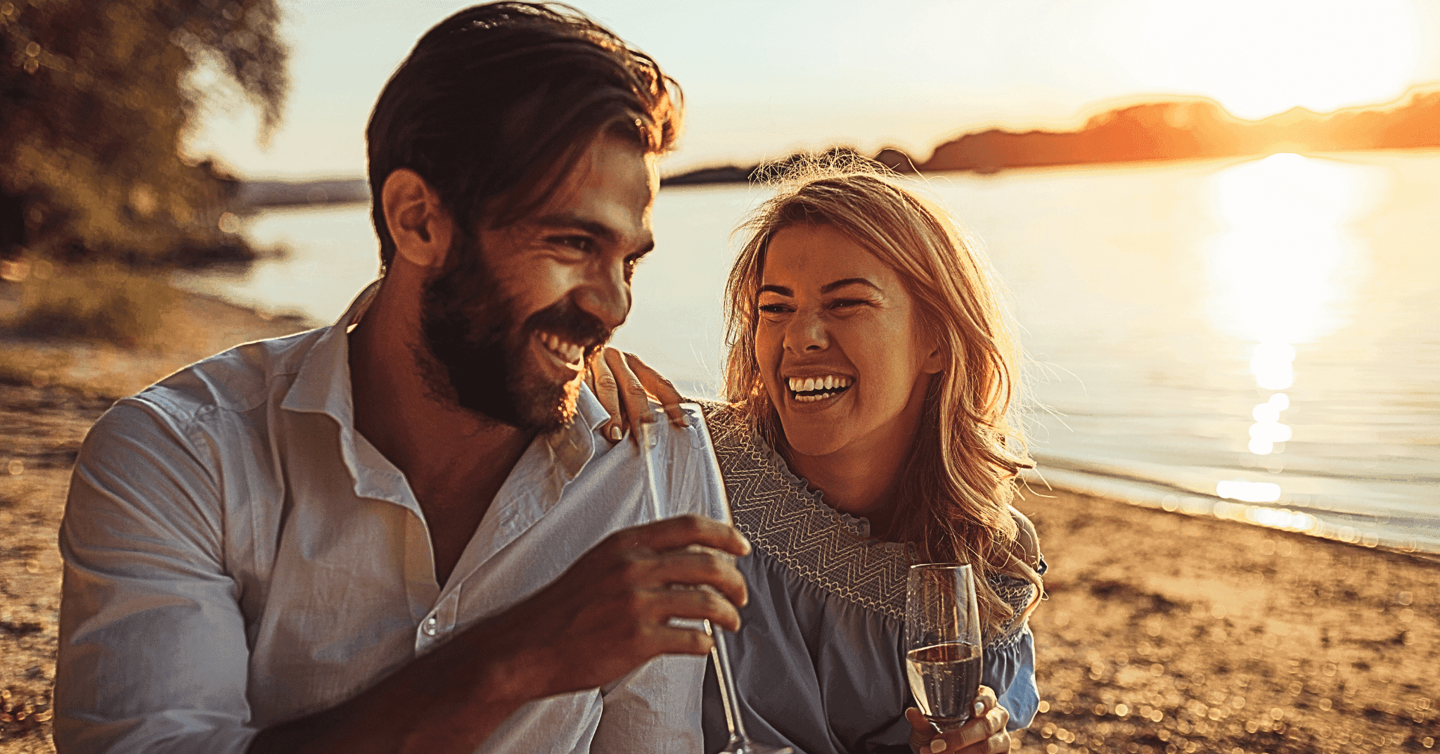 et glad par sidder på stranden med et glas champagne mens de nyder solnedgangen og hinandens selskab