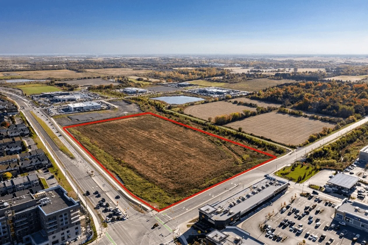 Aerial view of a large undeveloped parcel of land outlined in red at a busy intersection with nearby commercial buildings and residential areas. This real estate drone photography uses clear property outlining to define the lot boundaries, helping a drone photographer present development potential and location context to buyers.