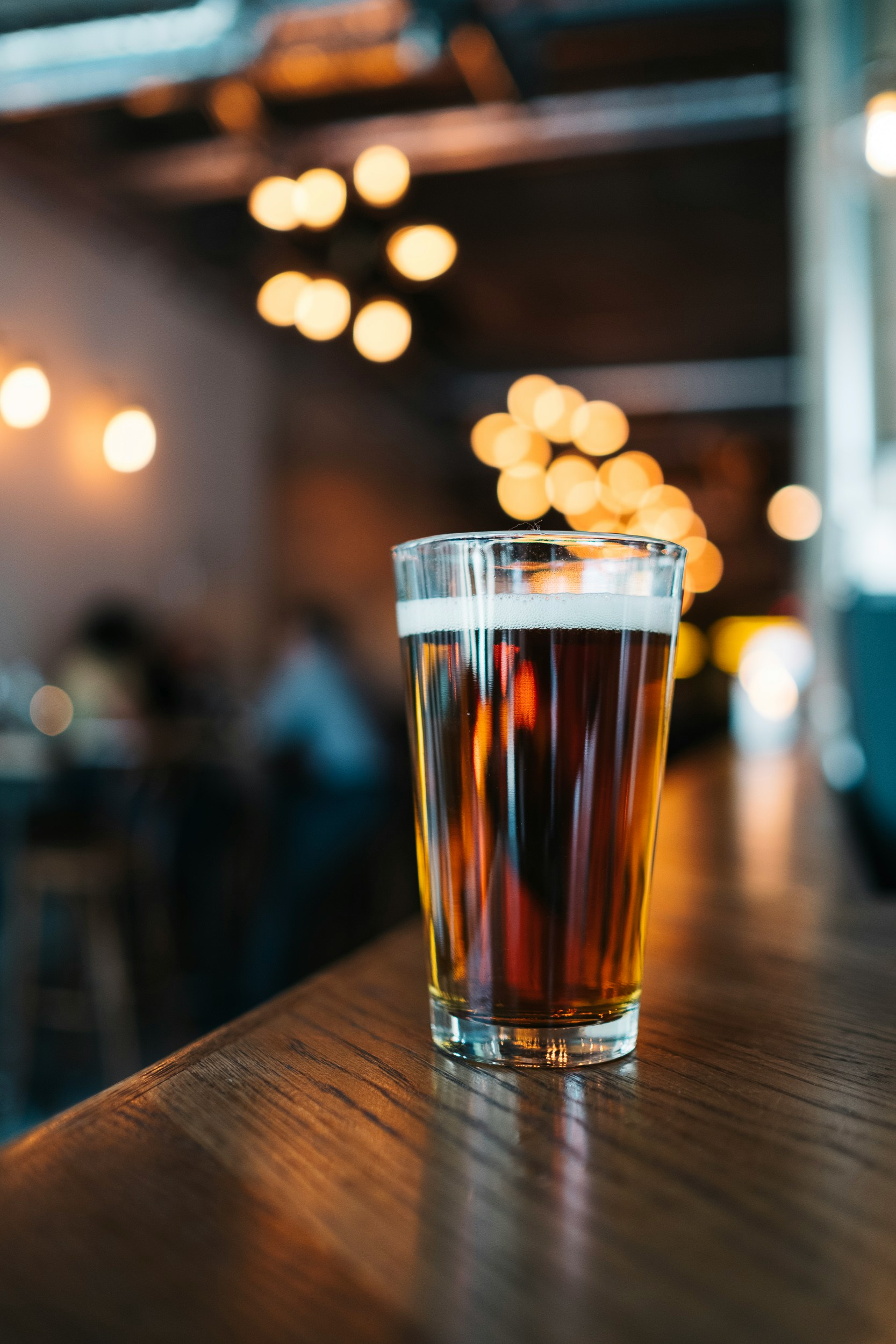 A glass of deep amber red beer on a bar with warm lights behind