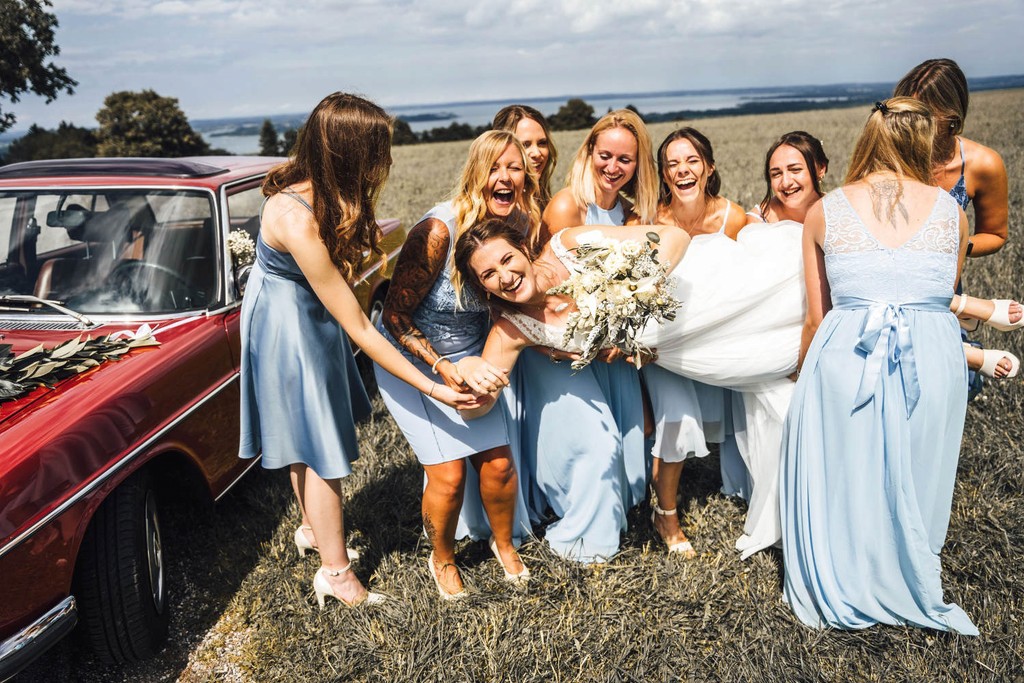 Braut wird von Freundinnen umringt und lacht während Hochzeit im Freien